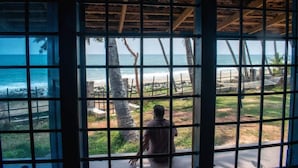 Una habitación con vista a la playa a través de una ventana con diseño de cuadrícula.