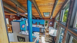 Une cuisine moderne avec des meubles bleus, un coin repas avec une table et des chaises en bois, et une vue sur l’extérieur grâce à de grandes fenêtres.