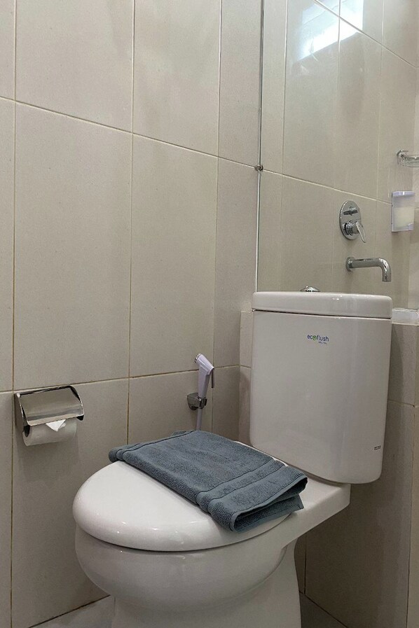 A bathroom with a toilet, a sink, and a toilet paper holder. - Binumar Guest House (Pekalongan)