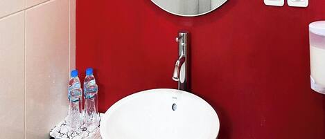 A bathroom with a white sink, a round mirror, and red walls.