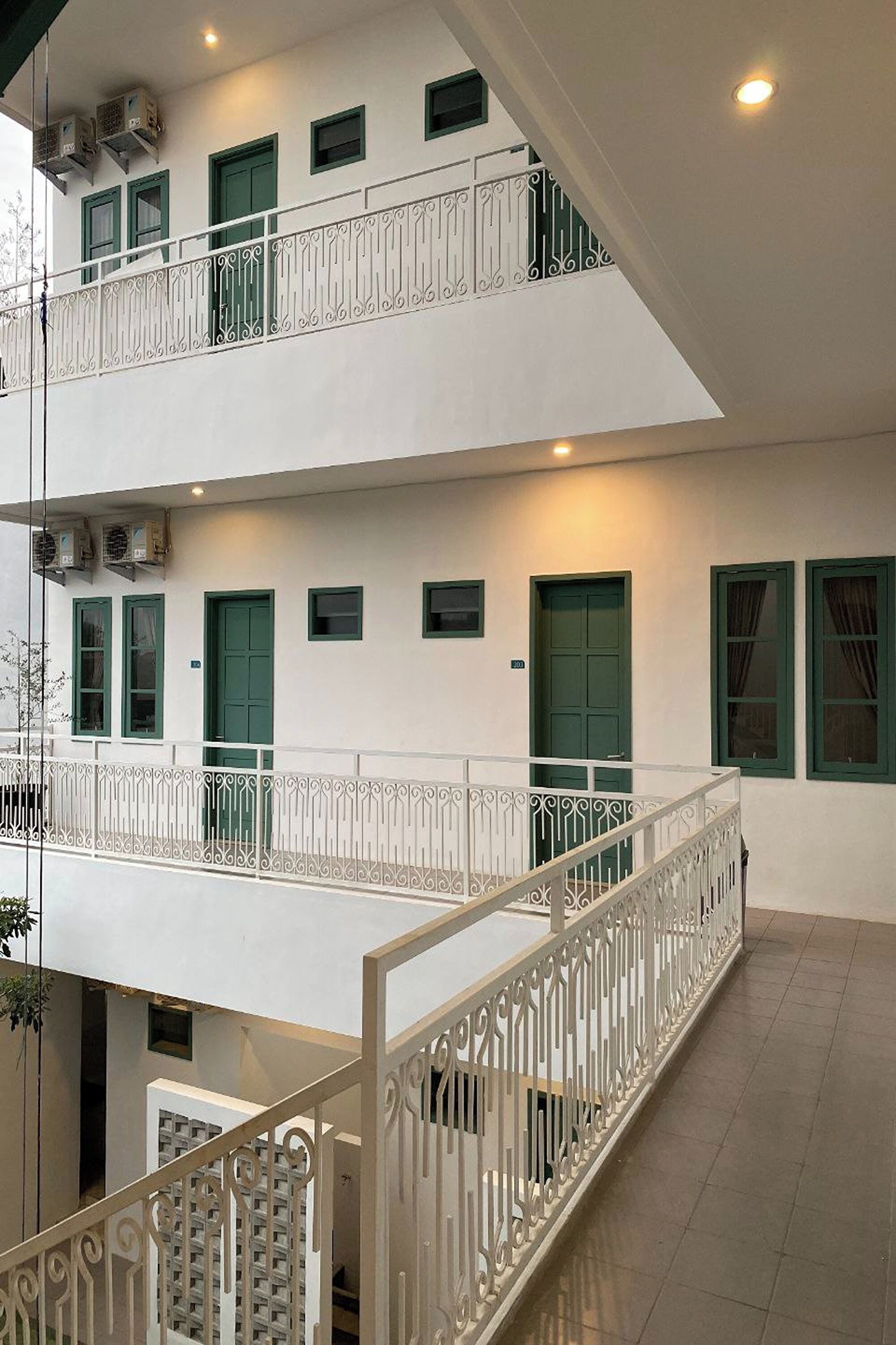 Un edificio de dos pisos con fachada blanca, puertas verdes y un balcón con barandillas blancas.