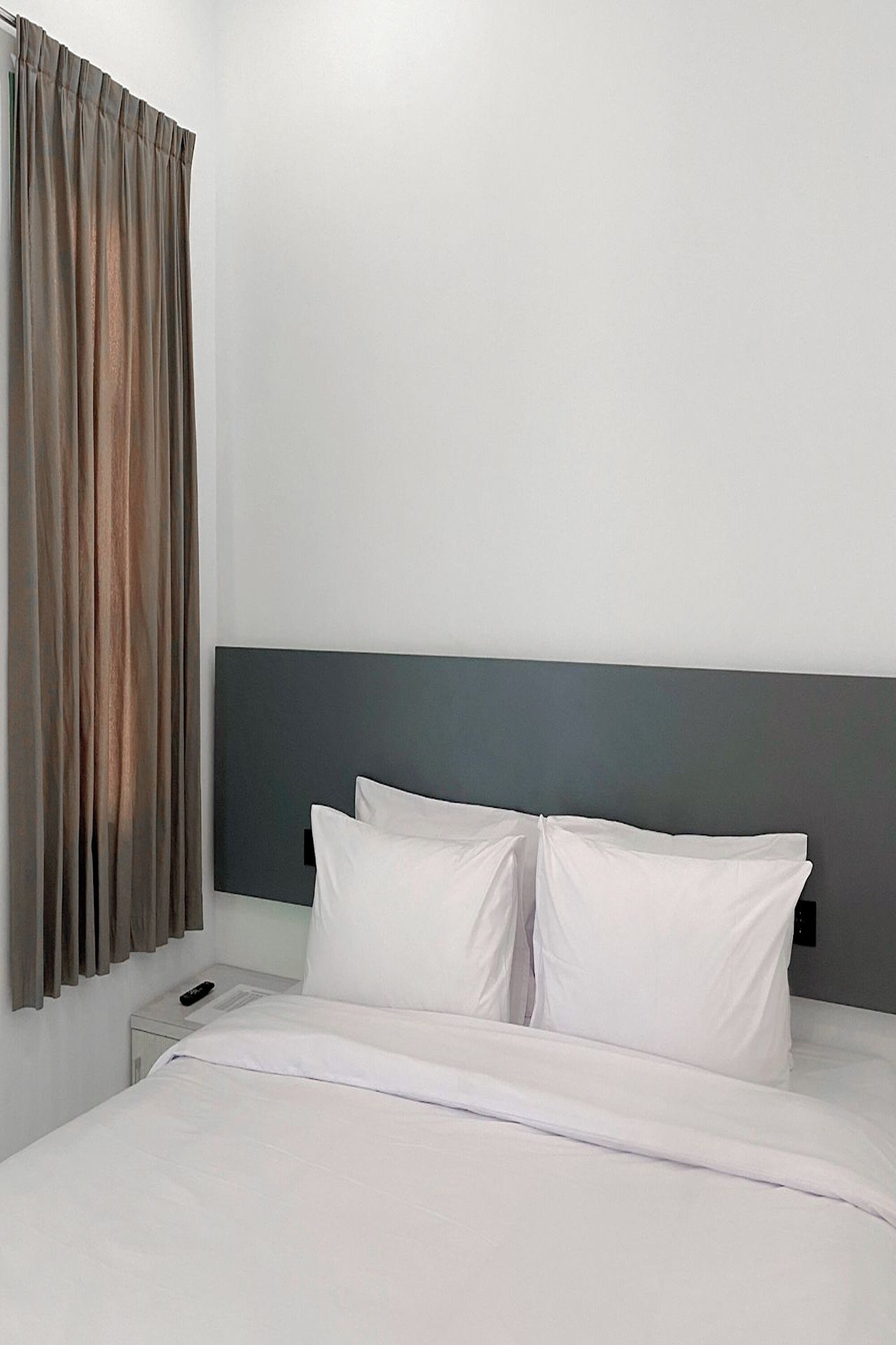 A neatly made bed with white linens, a grey headboard, and a remote control on the nightstand.