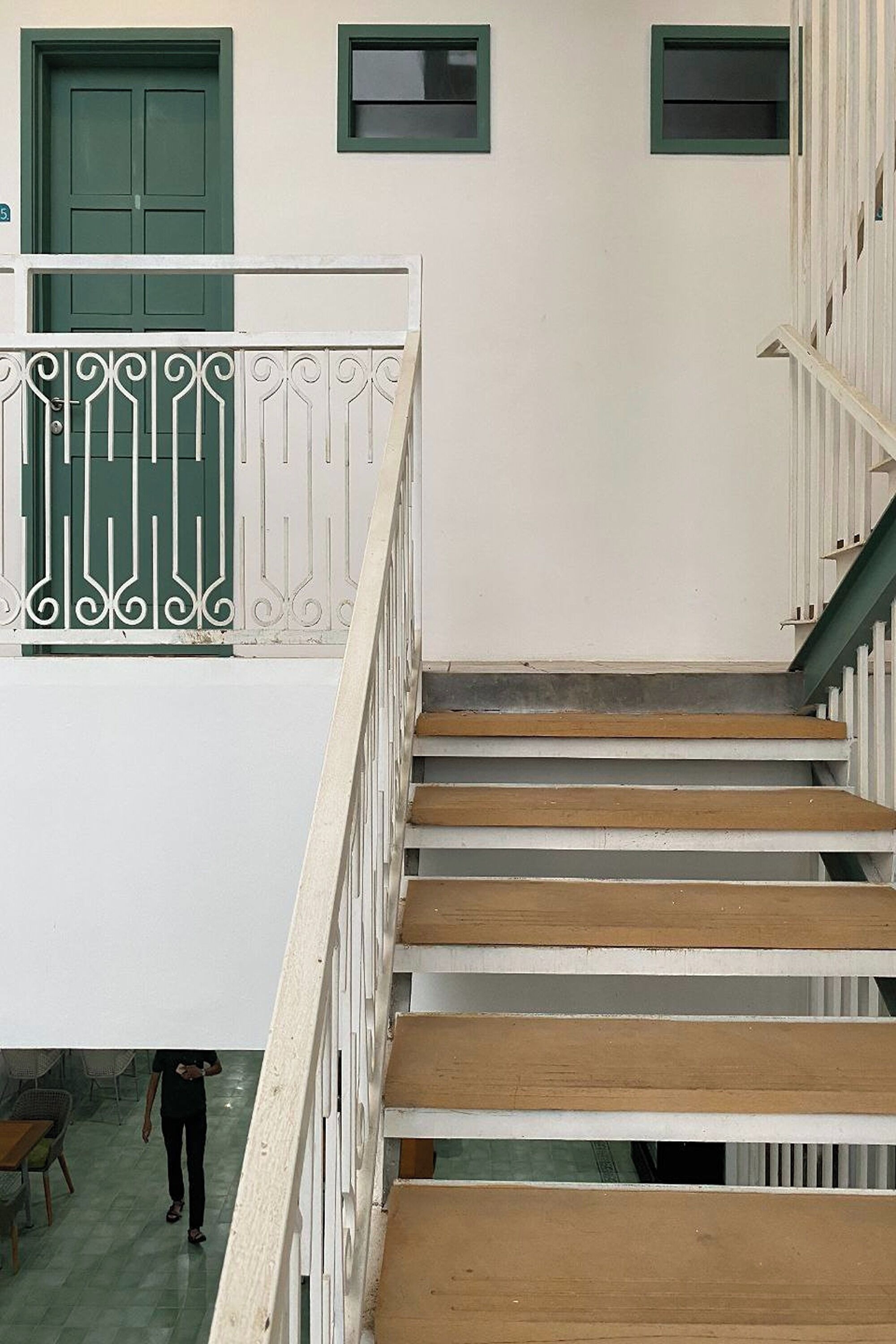Un escalier avec des rampes blanches et des marches en bois menant à une porte verte.