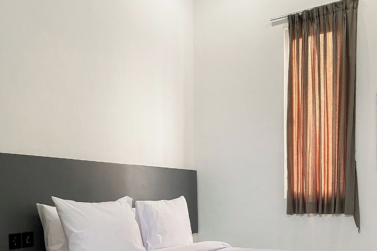 A modern hotel room with a large bed, a bedside table, and a window with curtains.