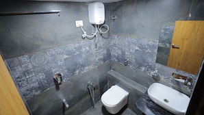 A modern bathroom with a toilet, bidet, and sink, featuring dark patterned tiles and a wooden door. - HOTEL R K FORTUNE (Gandhinagar)