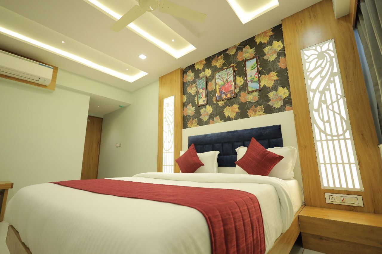 A hotel room with a large bed, a ceiling fan, recessed lighting, a window with a decorative screen, and a wall with framed artwork.