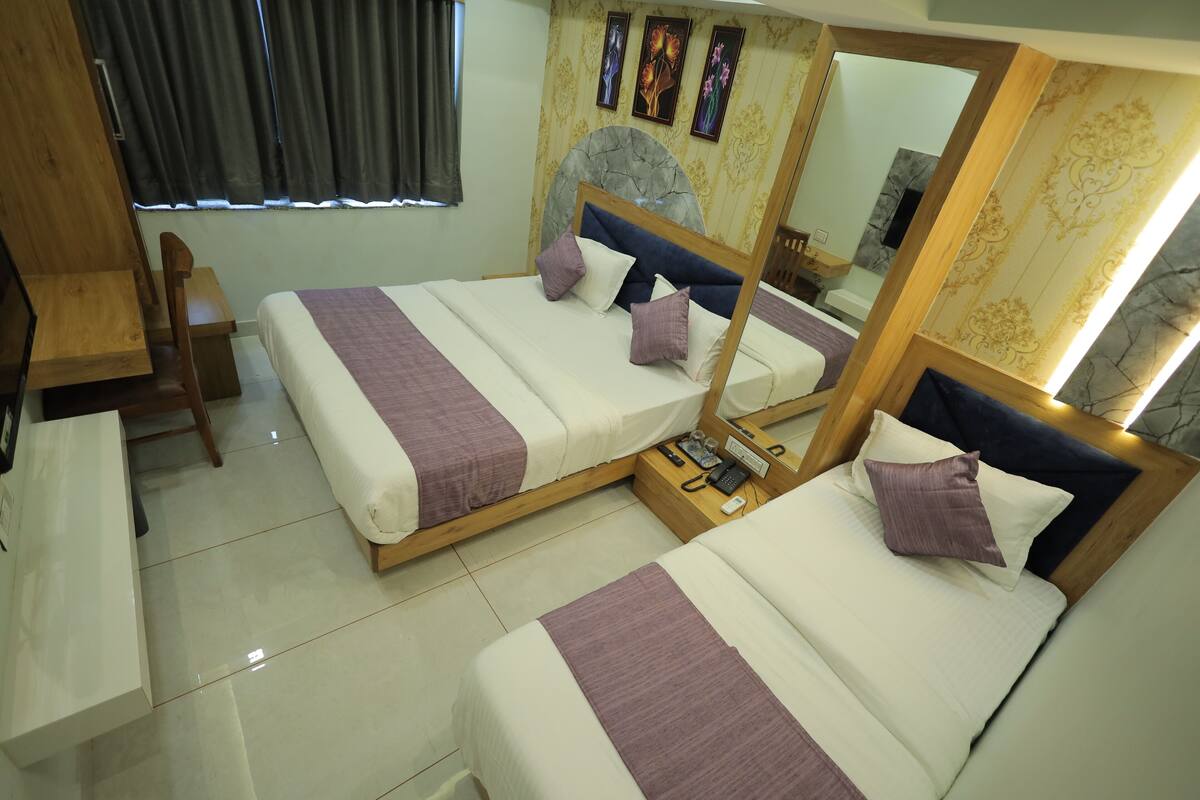 A hotel room with two beds, a wooden desk, a chair, a mirror, and a window with curtains.