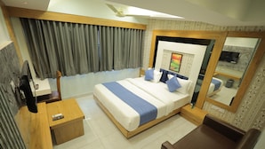 A modern hotel room with a large bed, a wooden desk, a mirror, and a TV. - HOTEL R K FORTUNE (Gandhinagar)