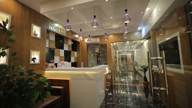 A hotel reception area with a wooden reception desk, pendant lighting, and a view of the hallway. - HOTEL R K FORTUNE (Gandhinagar)