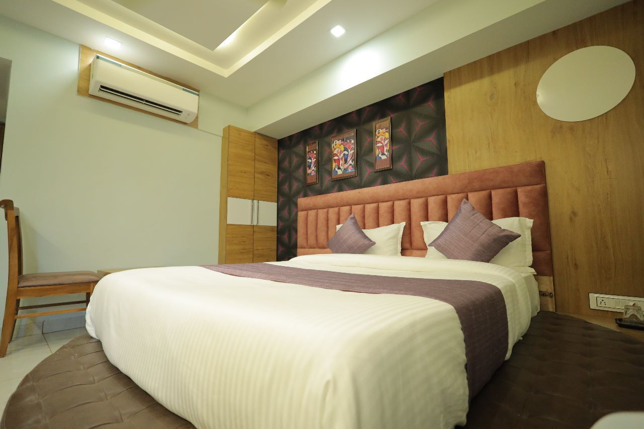 A neatly made bed with a headboard, a wooden chair, and a wall-mounted air conditioner.