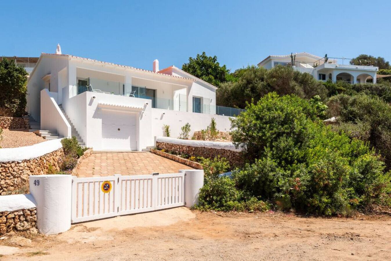 Eine moderne weiße Villa mit einer Steinsichtmauer, einem befahrbaren Eingangstor und freiem Blick auf die umliegende Landschaft.