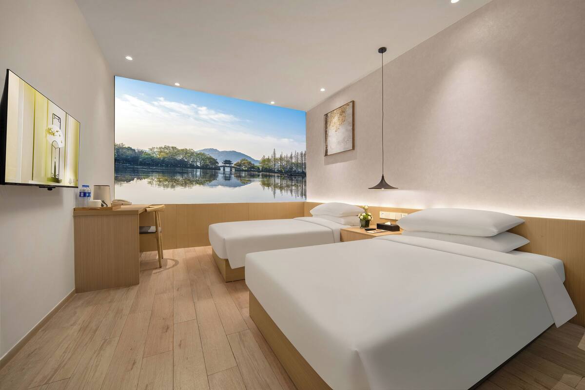 Habitació d'hotel amb dos llits, escriptori, cadira, televisió i una finestra gran amb vista a un llac.