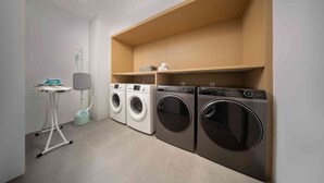 A laundry area with three washing machines, a small table, and a shelf with a few items. - Quantum Inn East Railway Station (Hangzhou)