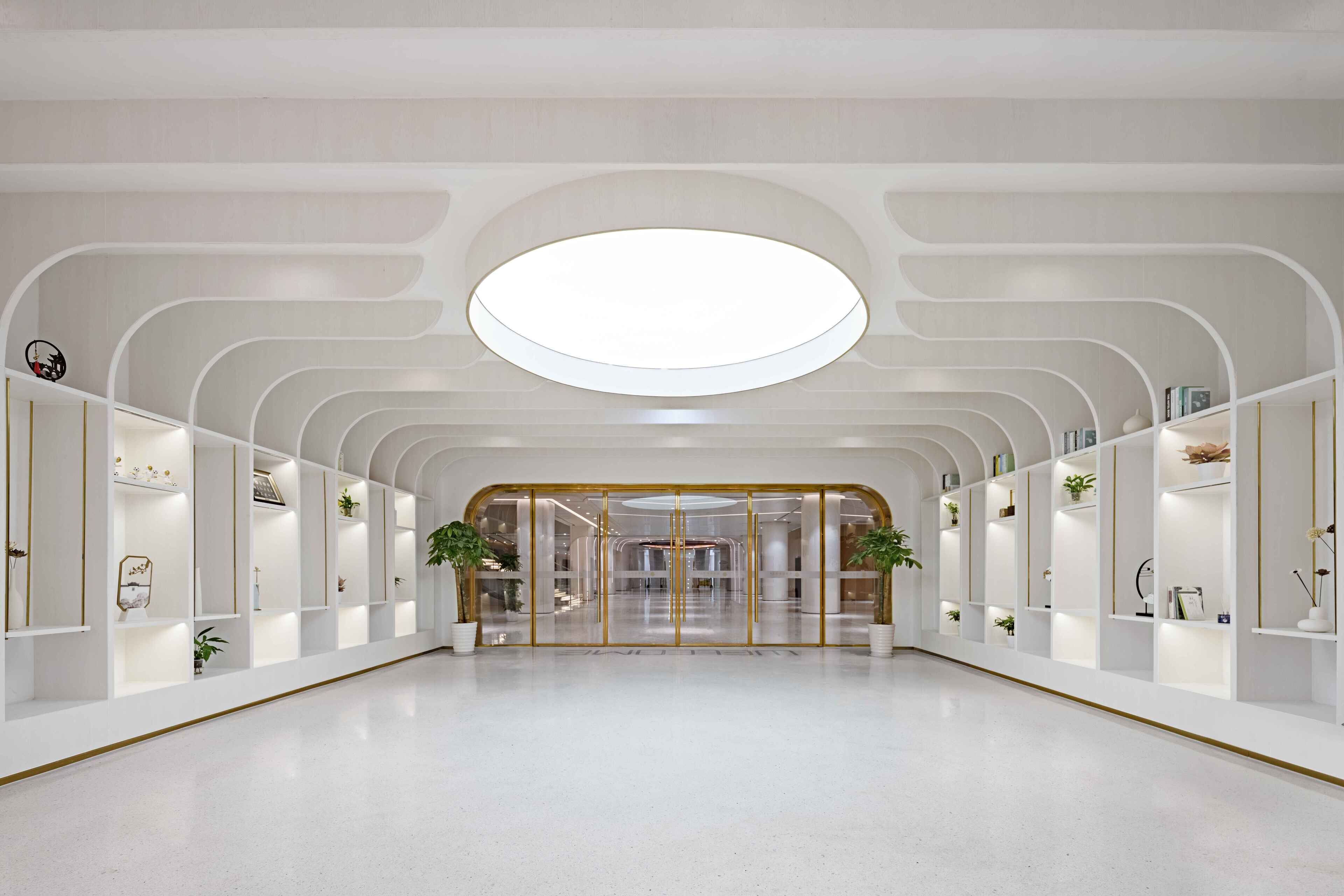 A spacious lobby with a central glass door, white walls, and a circular skylight.