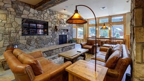A cozy interior with stone walls, leather furniture, a fireplace, and large windows. - 8045 Black Bear 1 Bedroom Condo by RedAwning (Keystone)