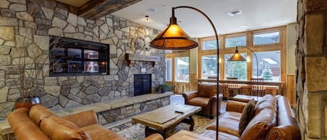 A cozy interior with stone walls, leather furniture, a fireplace, and large windows.