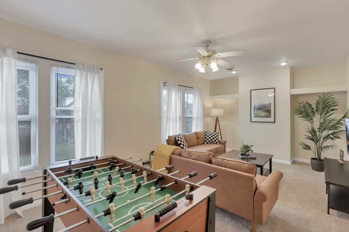 A living room with a foosball table, a ceiling fan, a sofa, a coffee table, and a potted plant.