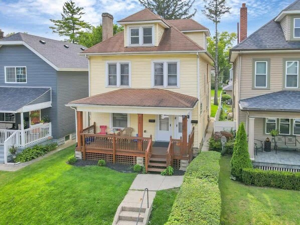 A two-story house with a front porch, a small deck, and a well-maintained lawn.