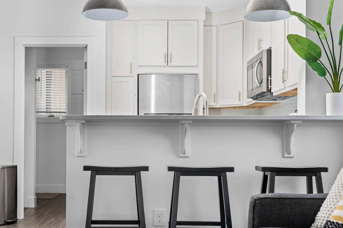 A modern kitchen with white cabinetry, stainless steel appliances, and a bar area with stools.