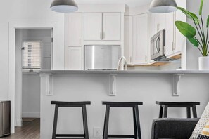 Uma cozinha moderna com armários brancos, eletrodomésticos de aço inoxidável e um espaço bar com banquetas.
