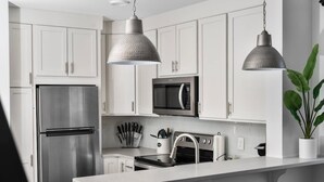 A modern kitchen with white cabinetry, stainless steel appliances, pendant lighting, and a potted plant.