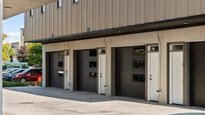 A modern building with a flat facade, multiple garage-style entrances, and a parking area with several cars.