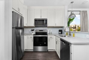 Uma cozinha moderna com armários brancos, eletrodomésticos de aço inoxidável e uma janela com vista para edifícios.