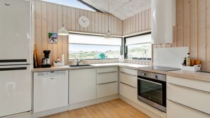 A modern kitchen with wooden paneling, a dishwasher, an oven, and a window with a view of the outdoors.