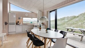 A modern kitchen with a large dining table, black chairs, and a view of the dunes outside.