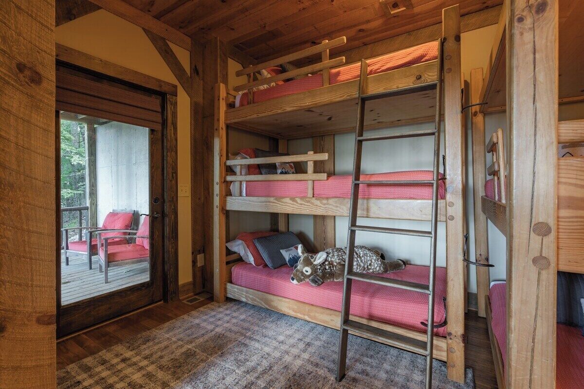 A cabin interior with bunk beds, a wooden ladder, and a view of a deck outside.