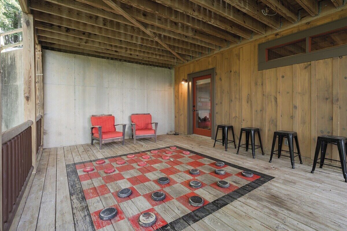 A wooden deck with a checkered floor, two red chairs, and four black stools.