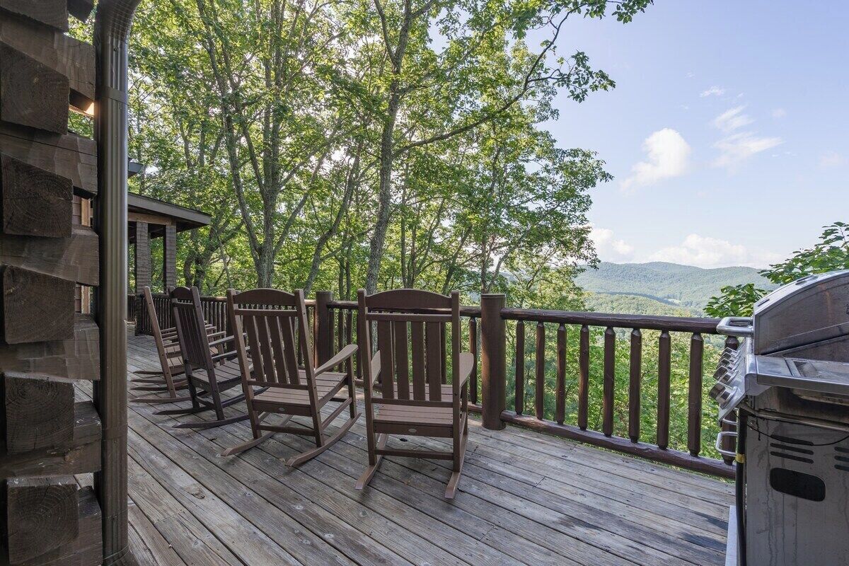 A wooden deck with rocking chairs and a grill, overlooking a forested area.