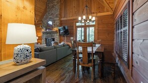 Een gezellig cabin interieur met een stenen openhaard, een eettafel met stoelen, een bank en een televisie.