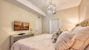 A bedroom with a large bed, a television on the wall, a dresser, and a chandelier.