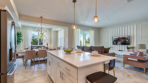 A modern kitchen with a large island, dining area, and a living room with a sofa and TV.