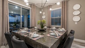 Ein Esszimmer mit Glastisch, sechs Stühlen, einer Blumenvase und einer Deckenleuchte.