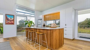 Eine moderne Küche mit einer Holztheke, Barhocker und einem großen Fenster mit Blick ins Freie.