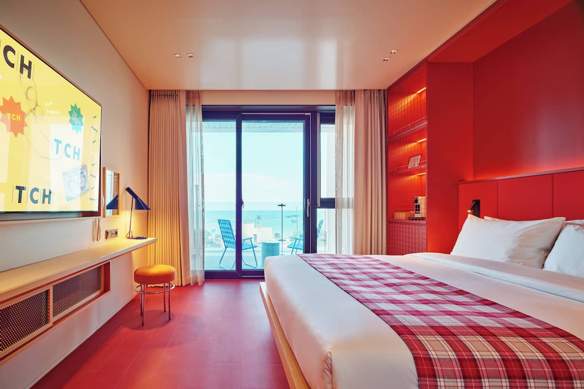 Habitación de hotel con cama, escritorio, silla, ventana grande y una pared de acento roja.