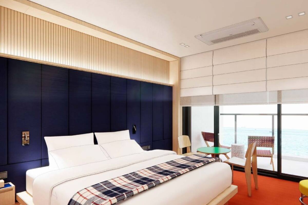 Una habitación de hotel moderna con una cama grande, vista al mar y un balcón con sillas.