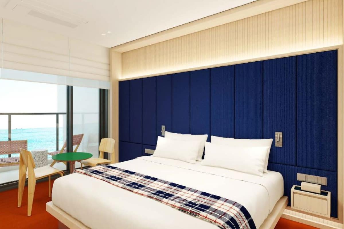 Habitación de hotel moderna con una cama grande, vistas al mar y un balcón con mobiliario.