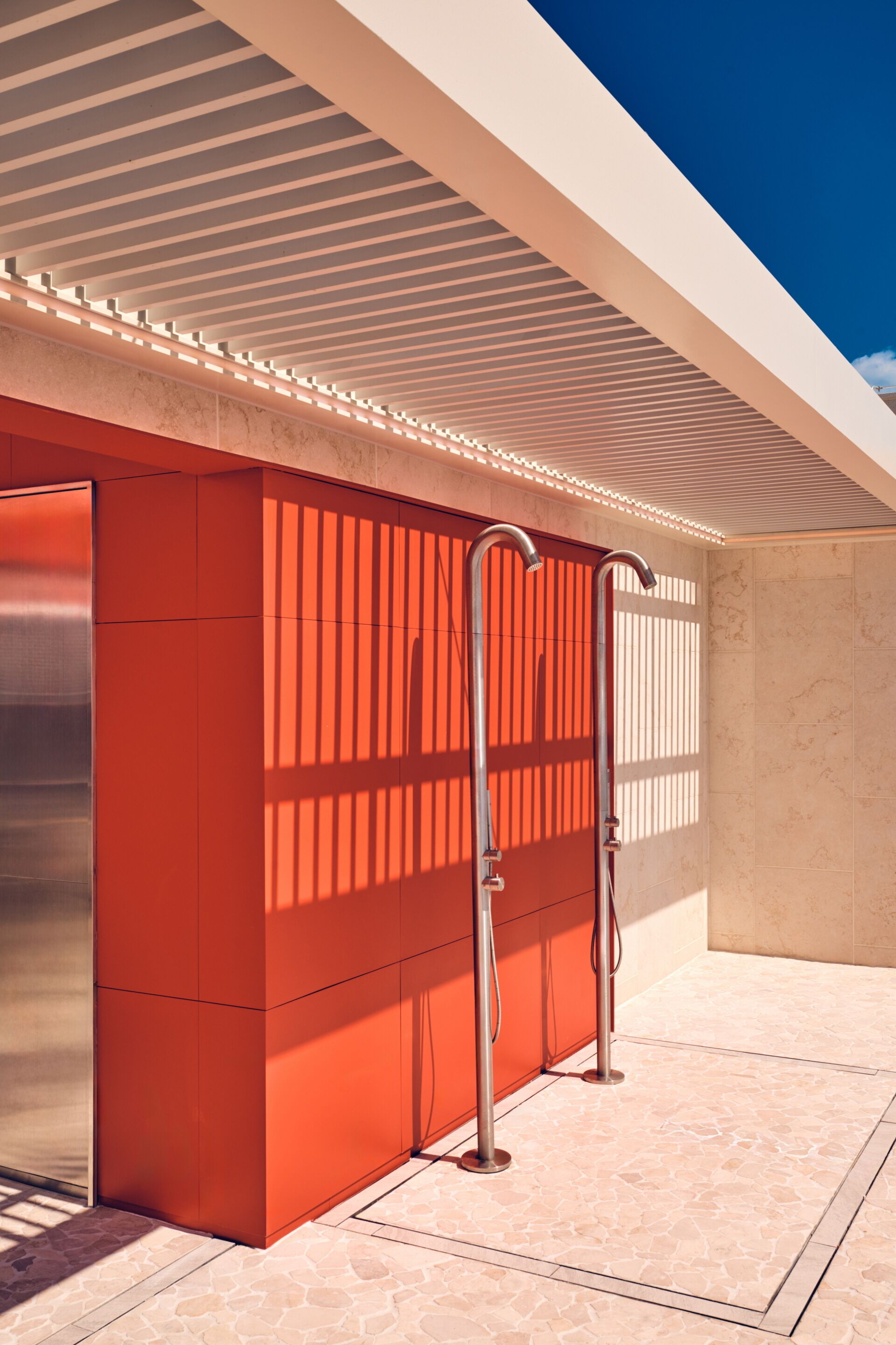 A modern bathroom with a red accent wall, a shower area, and a ceiling with a linear light design.