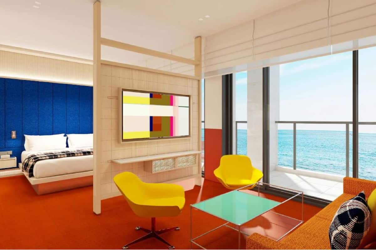 Un hotel moderno con una cama, un cuadro abstracto colorido, una silla amarilla, una mesa de vidrio y vistas al mar.