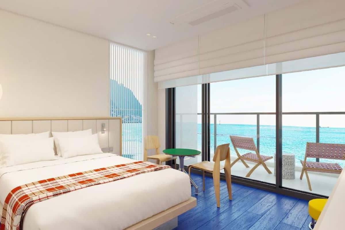 Una habitación de hotel moderna con una cama grande, vistas al océano y un balcón con sillas.