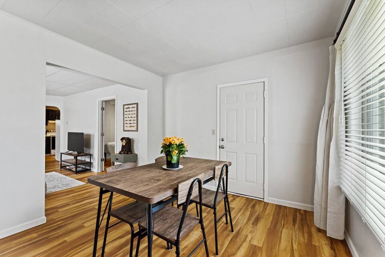Un comedor con una mesa y sillas de madera, un jarrón de flores y una puerta blanca.