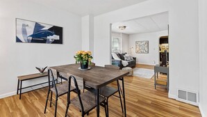 A modern living room with a wooden dining table, chairs, and a sofa. There is a painting on the wall and a plant on the table. - Pattison`s Peaceful Retreat (Superior)
