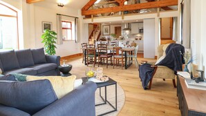 A spacious living area with a high ceiling and exposed wooden beams, a dining area with a wooden table and chairs, and a kitchen in the background. - Rowtor (Matlock)