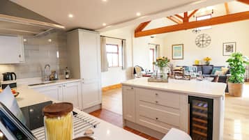 Una cocina moderna con armarios blancos, horno empotrado e isla central con enfriador de vinos.