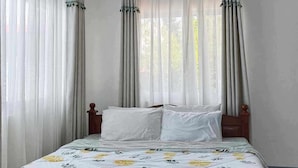 A bedroom with a bed, white curtains, a floral bedspread, and a ceiling light fixture. - Villa Tomasa Virgin Hotel (Panglao)