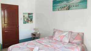 A bedroom with a bed, a painting, a door, and a small table. - Villa Tomasa Virgin Hotel (Panglao)