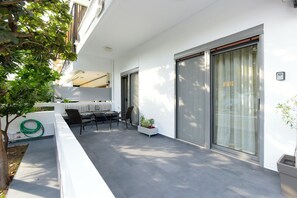 Une terrasse extérieure moderne, avec une table et des chaises, une plante en pot et une porte-fenêtre coulissante.